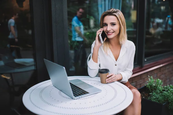 Glada Kvinna Tittar Kameran Och Talar Mobilen Medan Sitter Vid — Stockfoto