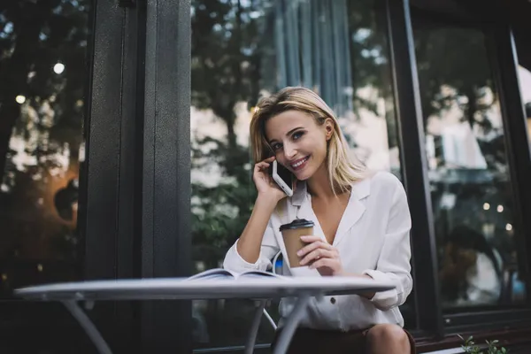下面是穿着休闲装的满意女性白天边喝咖啡边用智能手机聊天去户外咖啡店的照片 — 图库照片
