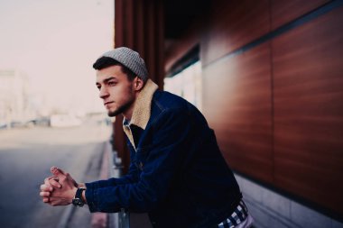 Sıcak ceketli ve bereli modern sakallı bir erkek. Düşünceli bir şekilde şehrin terasında duruyor.