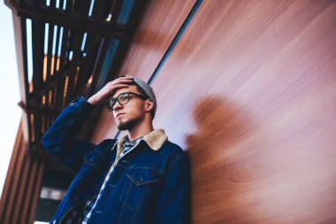 Dalgın sakallı, sıradan kıyafetli hippi bir adam ahşap duvarın yanında dikilip saçlarına dokunurken yüzünü çeviriyor.