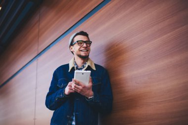 Düşük açılı, gri şapkalı ve gözlüklü genç bir erkek. Mesajları kontrol ederken ekrandan uzağa bakıyor.