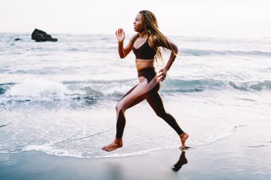 Motive olmuş kadın koşucu sabah rutin eğitim gücü ve dayanıklılığı boyunca sahil şeridinde koşuyor, kararlı sportif kadın aktif yaşam tarzını ve mükemmel vücut şeklini korumak için kardiyo çalışması yapıyor.