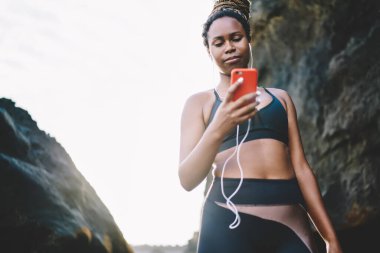 Milenyum esmer tenli, elektronik kulaklıklı, spor sitesine girip akıllı telefondan online eğitim alan, cep telefonu teknolojisiyle mesajlaşan Afro-Amerikalı bir kadın.