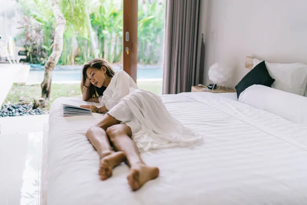 亚洲女人穿着睡衣 躺在舒适的床上 细心地看书 白天一个人在舒适的卧室里放松 — 图库照片