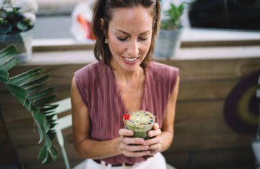 Moda kıyafetleri içinde, egzotik yeşil smoothie kadehlerine bakan ve gündüzleri açık hava restoranında dinlenen yetişkin bir kadın.