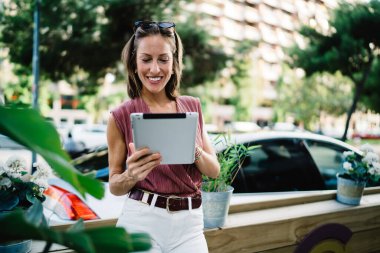 4G bağlantısı üzerinden tablet üzerinde bilgi arayan ve paylaşan neşeli beyaz kadın, açık kafedeki terasta oturmuş dijital tablette kitap okuyan gülümseyen kadın.