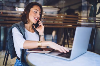 Kafkas kadın blogcu laptopta yazı yazıyor kafeterya terasında uzaktan iş yapıyor, akıllı telefonda gülümseyen bir kadın internet projesini tartışırken teknolojiyi kullanıyor.