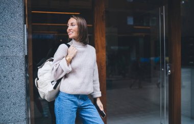 Sırt çantalı ve gülümseyen mutlu Kafkasyalı turist seyahat tatillerinden memnun, 30 yaşındaki neşeli kadın şehir merkezinde durmuş tatillerde uluslararası yolculuğun keyfini çıkarıyor.