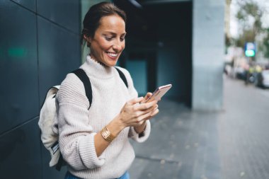 Sırt çantalı dişlek gezgin kız solo tatillerde online mesajlaşma için modern hareketlilik teknolojisini kullanıyor, neşeli kadın mesajlar alıyor ve uluslararası gezintiye bağlanarak gülümsüyor.