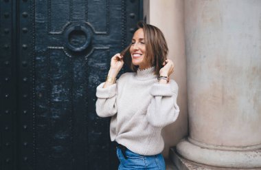 Şık giyinmiş şık bir kadın şehrin antik kapılarının yanında duruyor ve tek başına seyahat eden neşeli beyaz modelle gülüyor rahat kış süveteri giymiş neşeli.