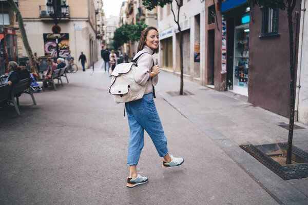 Веселая женщина с рюкзаком для путешествий, гуляющая по улицам города во время отдыха в одиночку для посещения новых мест, радостная женщина, осматривающая город и смеющаяся во время весеннего досуга