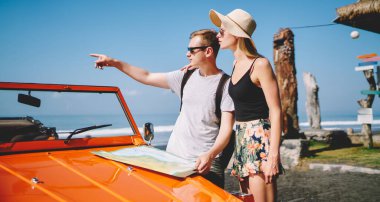 Yandan bakan bir adam, omuz omuza tutuşan bir kız arkadaş, elinde haritayla tatilde gideceği yeri belirleyen bir araba.