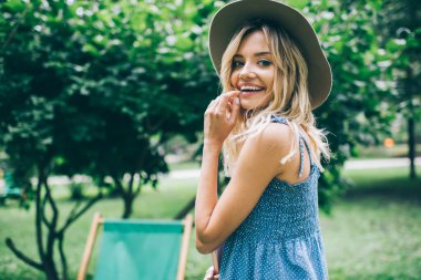 Moda şapkalı mutlu hippi kızın yarım boy portresi. Parkta güzel bir gündüz vakti kameraya gülümsüyor. Şık giyinmiş neşeli bir bayan turist.