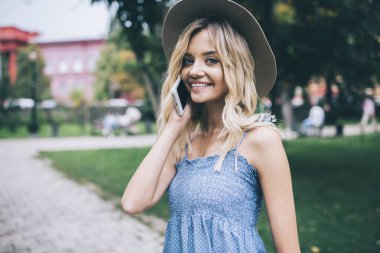 Kameraya gülümseyen neşeli bayan turistin yarım boy portresi gezici, modaya uygun şapkalı mutlu hippi kızla sohbet ederken boş zamanlarında akıllı telefon iletişiminin keyfini çıkarıyor.