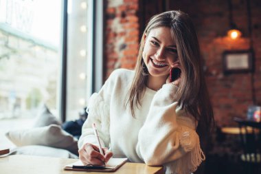 Gülen serbest çalışan kadın, panoya notlar yazıyor ve kafede çalışırken cep telefonuyla sohbet ediyor.