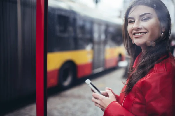 スマートフォンでバスやサーフィンのインターネットを待っているカメラを見て歯の笑顔で幸せな女性のガラスを通して — ストック写真
