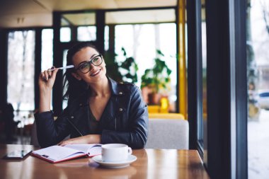 Genç, mutlu, uzaktan kumandalı, dişlek gülümsemesi olan, dişlek bir kadın işçi. Başka tarafa bakıyor ve iş günü için yeni bir proje düşünüyor.