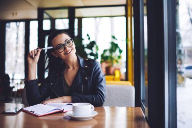 Genç, mutlu, uzaktan kumandalı, dişlek gülümsemesi olan, dişlek bir kadın işçi. Başka tarafa bakıyor ve iş günü için yeni bir proje düşünüyor.