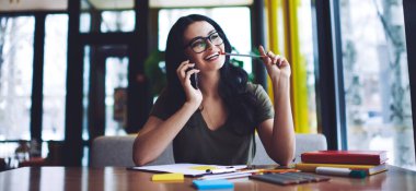 Günlük kıyafetler ve gözlüklerle gezen neşeli genç bir kız öğrenci. Proje hazırlıkları sırasında cep telefonuyla konuşuyor ve başka yere bakıyor.