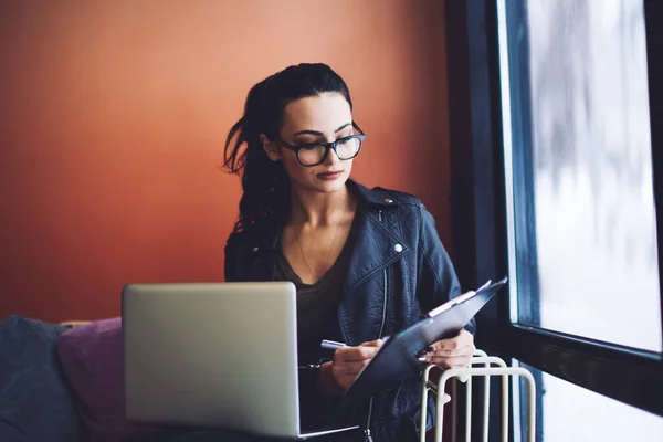 Pensive Uczennica Ubraniach Casual Okularach Pisanie Notatek Papierze Schowku Podczas — Zdjęcie stockowe