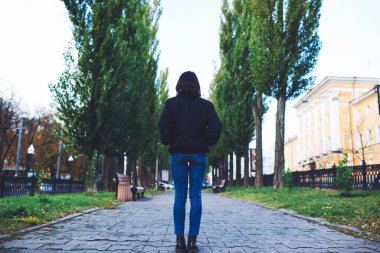 Siyah ceketli ve kot pantolonlu genç bir bayanın arka görüntüsü.