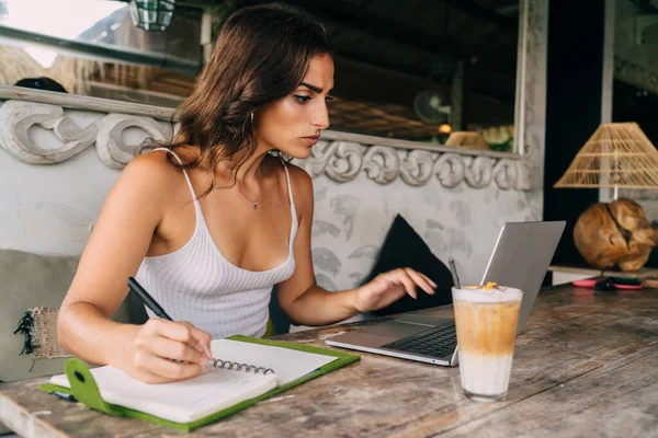 在夏季以年轻女作家为重点 在笔记本电脑上学习信息 边做文章边做笔记 边坐在时尚的户外咖啡馆里喝冷饮 — 图库照片