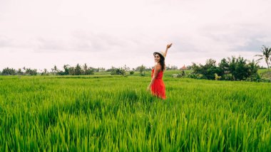 Kırmızı elbisesi ve şapkası olan, vadide yürüyen ve kameraya bakıp gülen olumlu bir kadın.