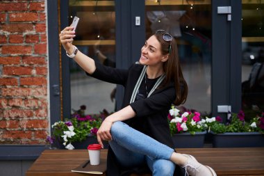 Boş zamanlarında selfie çeken mutlu Kafkasyalı bir kadın açık havada mobil uygulama kullanıyor, günlük kıyafetlerle gezen neşeli hippi kız şehirdeki boş zamanlarında telefon kamerasına gülümsüyor.