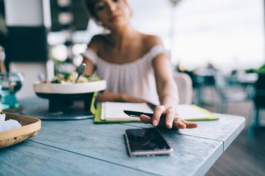 Yazın üstten arama yapan ekin dişisi servis tabağı ve defter ile açık kafe masasında otururken cep telefonuyla arama yapıyor.