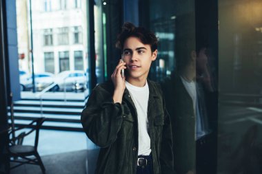 Açık kafede camdan duvara yaslanmış ve molada cep telefonuyla konuşan genç bir adam gözlerini kaçırıyor.