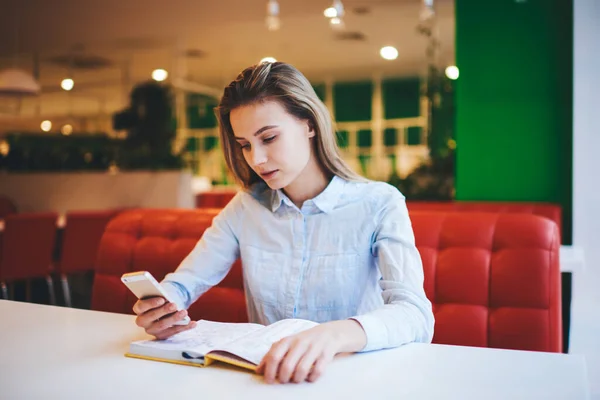 Pensive Female Casual Clothes Sitting Table Opened Book Browsing Mobile — Stock Photo, Image