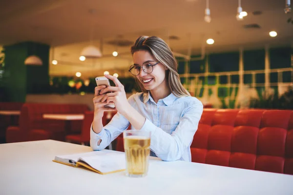 Fiatal Boldog Alkalmi Ruhákban Fogas Mosollyal Asztalnál Ebédlőben Mobiltelefont Használ — Stock Fotó