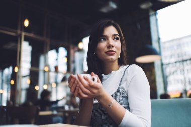 Uzun siyah saçlı, genç bir kadın. Teneffüste sıcak kahveyle rahat koltukta otururken gözlerini kaçırıyor.