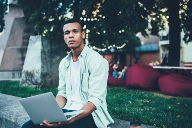 Ciddi bir Afro-Amerikalı genç adam internette internette gezinirken yaz akşamları dinleniyor.