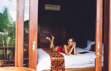 Mayo giymiş keyifli bir kadın turist. Evin yumuşak yatağında uzanıyor. Yaz tatilinin tadını çıkarıyor.