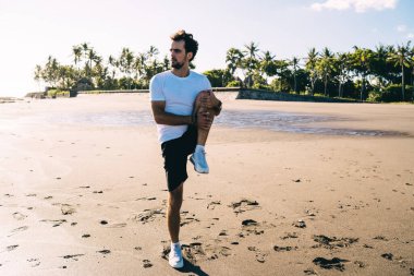 Uzun boylu, sakallı bir adam spor giyer ve antrenmandan önce Palm 'ın yakınındaki kumsalda ısınırken yüzünü çevirir.