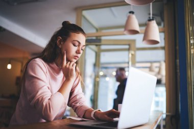 Laptop 'ta yazı yazan ve arka planda bulanık duran genç, düşünceli bayan yöneticinin yan görüntüsü.