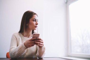 Düşünceli genç bayan pencerenin yanındaki masada otururken ve dinlenirken gözlerini kaçırıyor.