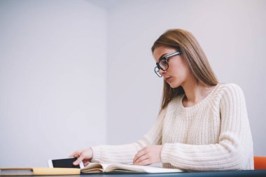 Masada oturup not defteri okuyup, cep telefonu alırken uzun saçlı, rahat bir bayan öğrenci.