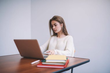 Düşünceli genç bayan gündelik kıyafetlerle modern netbook 'u karıştırırken ahşap masada belgelerle oturuyor ve gündüzleri çalışıyor.
