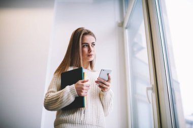 Fotokopi kitaplarıyla ve çağdaş akıllı telefonlarla sörf yaparken gündelik süveter giyen hayalperest genç bayanın altından.