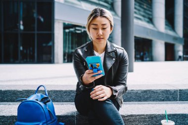 Milenyum Asyalı blogcu akıllı telefon teknolojisi aracılığıyla mesajları kontrol ediyor. Deri ceketli çekici bir kadın internet sitesi için 4G internete bağlanıyor.