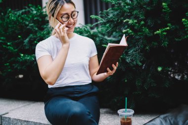 Eğitim kitaplarındaki neşeli bayan öğrenci uluslararası cep telefonu konuşmaları sırasında organizasyon planlayıcısını tartışıyor, gözlüklü mutlu Çinli kadın arkadaşça sohbetten zevk alıyor.