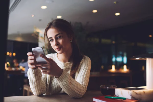 穿着暖和毛衣 留着棕色头发的年轻女子坐在桌旁 在咖啡店里用手机聊天 保持冷静 — 图库照片