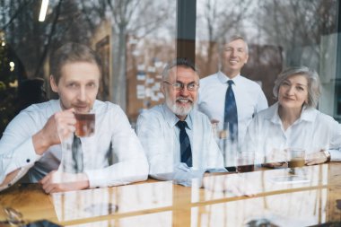 Resmi olarak bir bardak neşeli iş ortağının masasında oturup kahve içmesi ve kameraya bakması.