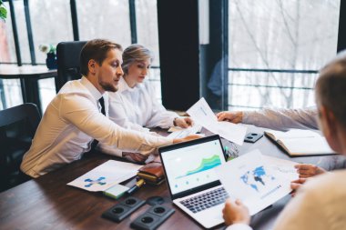 Yukarıdan gömlekli, ciddi iş ortakları kağıtları inceliyor ve ofiste toplanırken internet üzerinden bilgi topluyor.