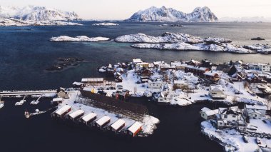 Geleneksel kırmızı Norveç evleriyle Lofoten balıkçı köyünün nefes kesici kuş bakışı görüntüsü. Fiyortlar arasında küçük şehir altyapısı olan panoramik ada manzarasının insansız hava aracı görüntüsü
