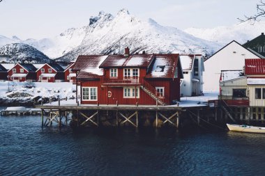 Norveç 'te arka planda karlı dağlarla kaplı Nordic Körfezi' nin karanlık sularının üzerindeki ahşap iskelede bulunan küçük kırmızı evin dışı.