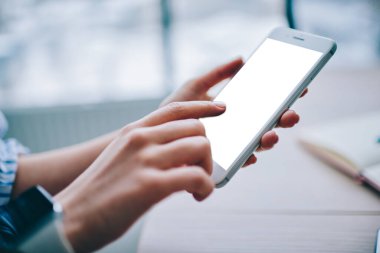 Yukardan gelen yüzü olmayan kişi, ahşap masadaki boş dokunmatik ekranlı ve not defterli modern cep telefonu kullanıyor.