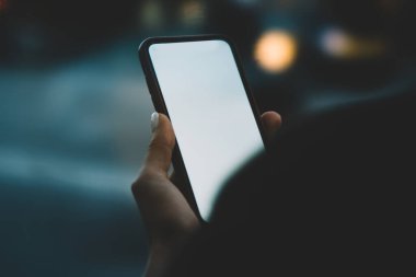 Günbatımında şehir caddesinde boş vakit geçirirken, yüzü olmayan stil sahibi kadın dijital cep telefonuyla e-kitap okuyor.